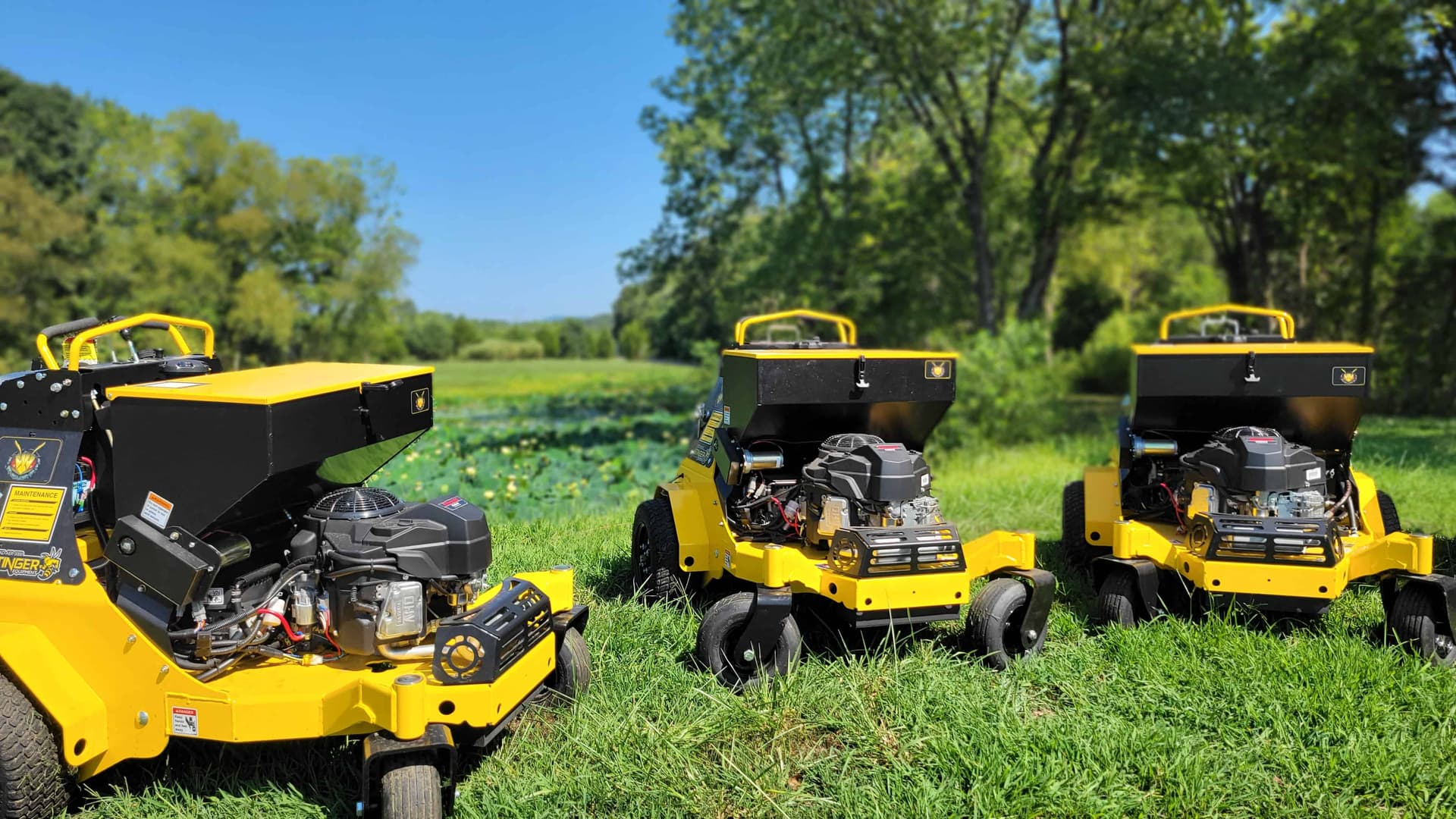 Three Simply Turf stand-on core aerators with seed boxes parked on a lawn