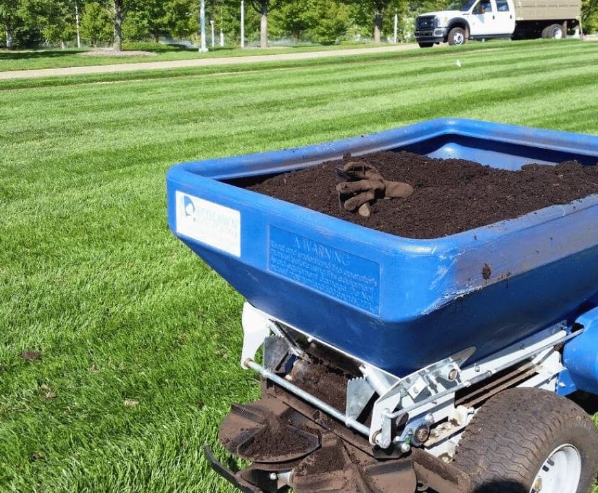 Blue compost topdresser loaded with screened compost on a striped lawn