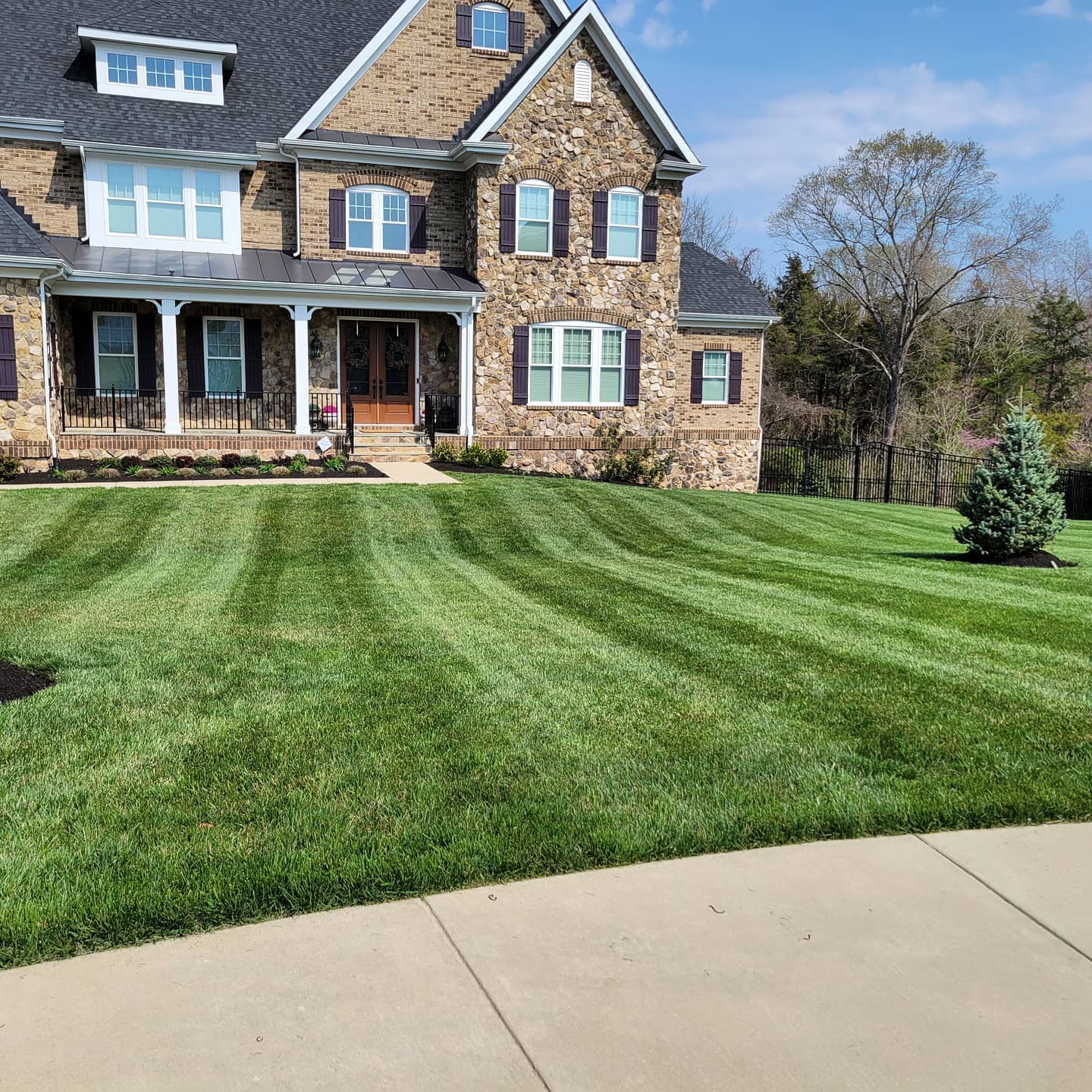 A thick, freshly striped weed-free front lawn in front of a Northern Virginia stone home