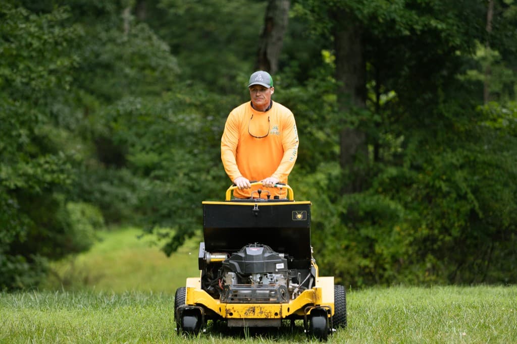 Simply Turf technician standing behind a stand-on aerator with seed box on a Northern Virginia lawn