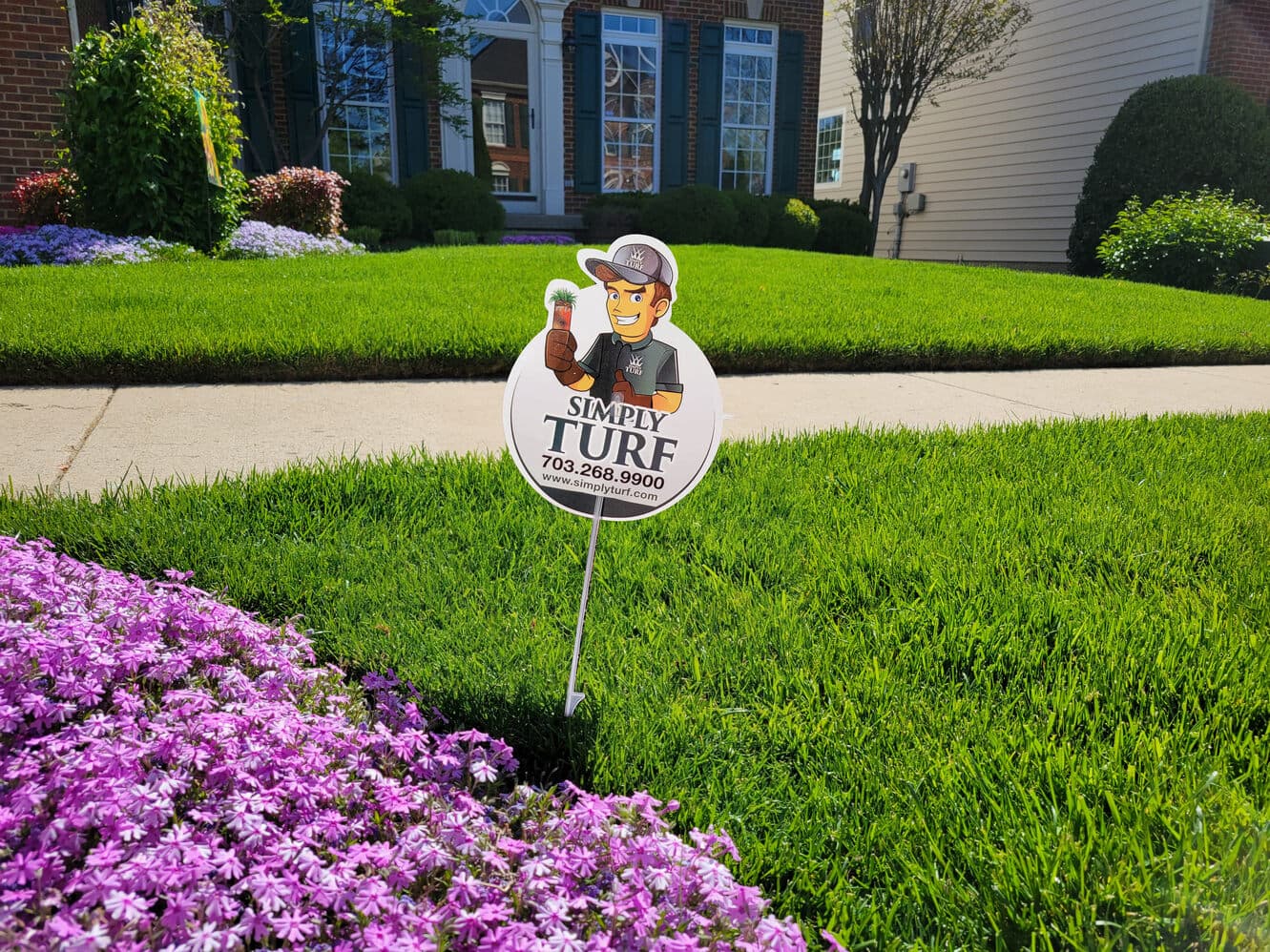 A healthy, weed-free lawn with a Simply Turf yard sign and pink flowers