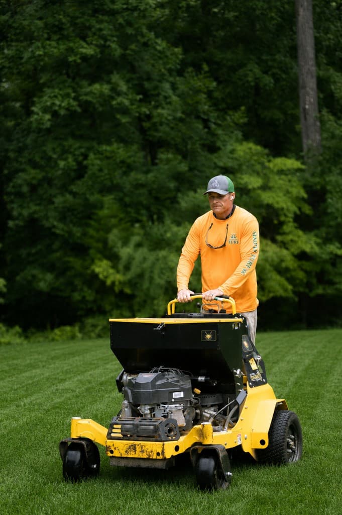 Simply Turf technician operating a Stinger stand-on core aerator on a Northern Virginia lawn