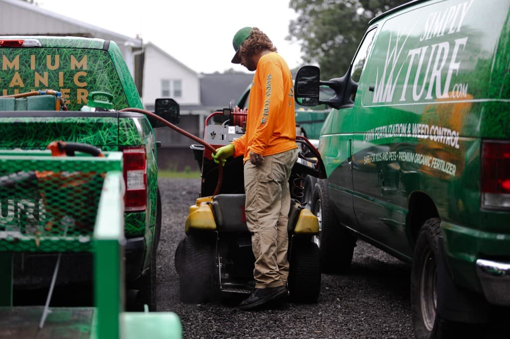 Simply Turf technician loading equipment between two Simply Turf service vehicles